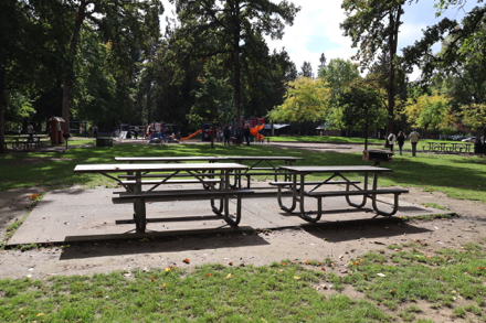 Four picnic tables, one with accessible extended end, located on concrete slab near playground – with grill – may have a lip